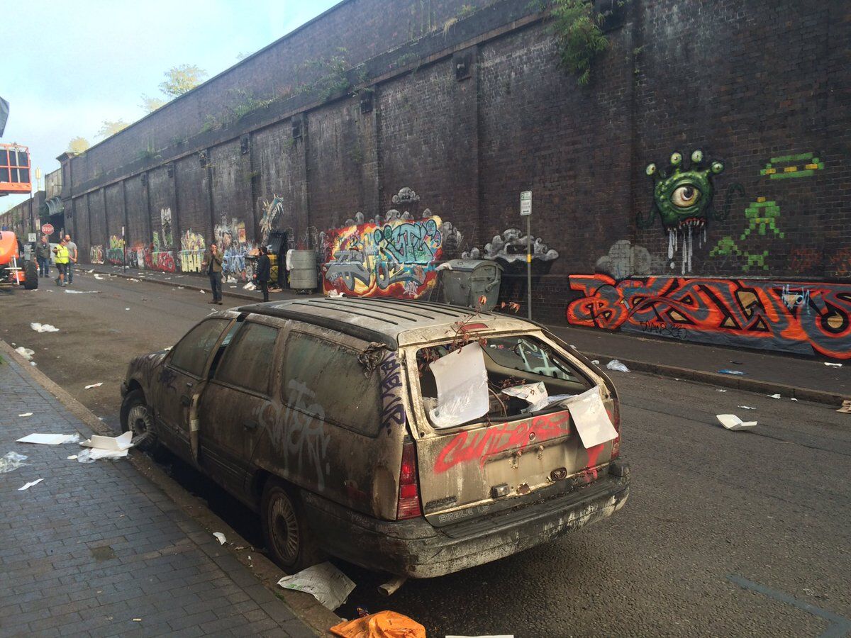 litter on the road with walls spray painted and broken dirty car