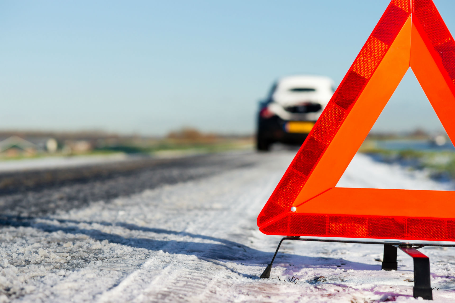 snowy road with warning triangle placed further behind a car